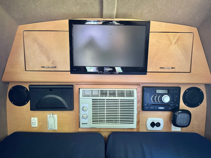 Interior of an RV rental: TV, AC unit, stereo, speakers, charging center, and other controls built into light wood cabinetry.
