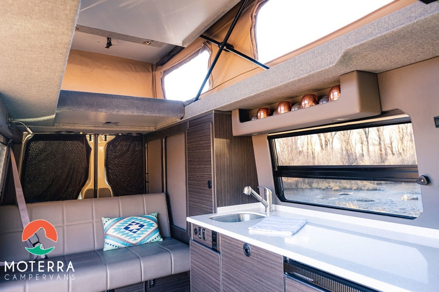 Experience an **rv rental** campervan: a modern interior with a pop-top bed, kitchen, and sofa, offering scenic views.