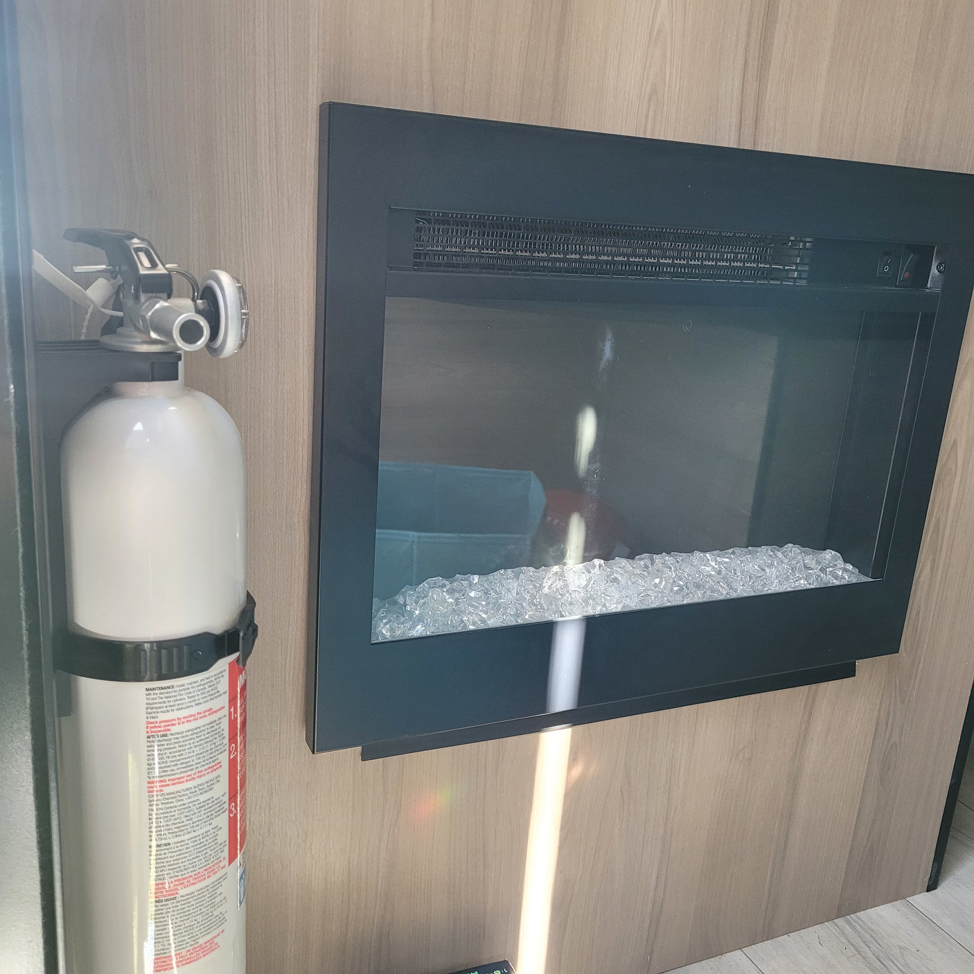 RV rental safety and comfort: a fire extinguisher mounted next to an electric fireplace with crystal media, set in a wood interior.