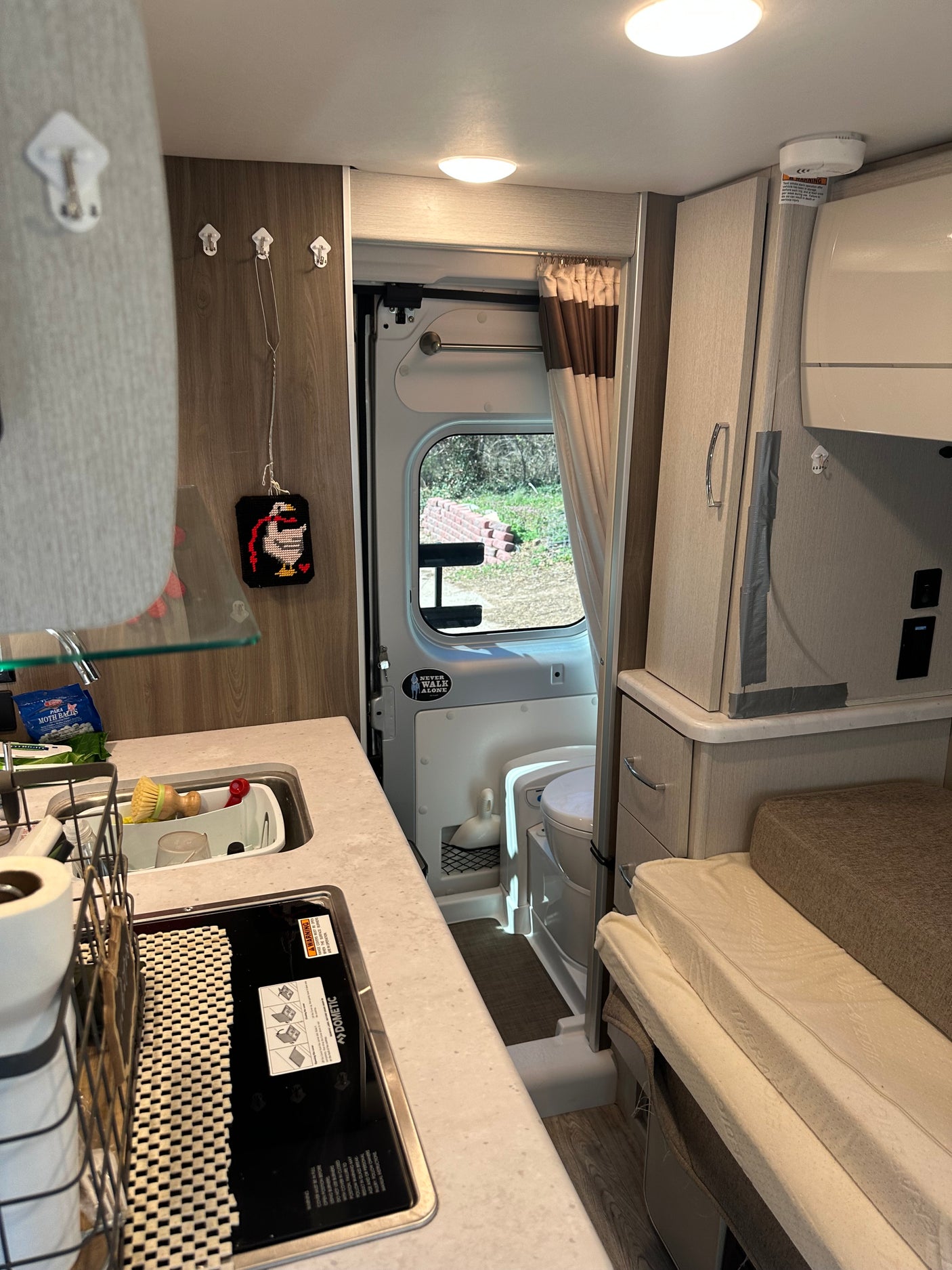 This RV rental interior reveals a compact galley kitchen (sink, Dometic stove), toilet in bathroom, and comfortable sleeping area.