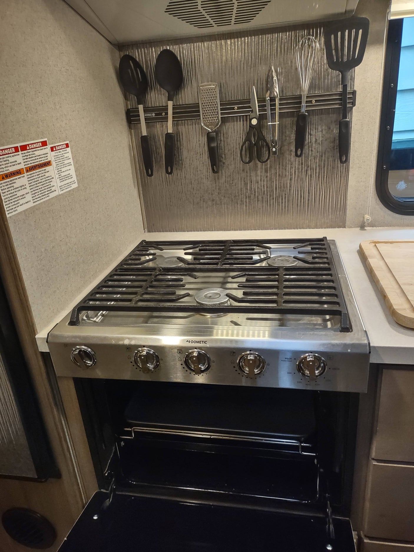 An RV rental kitchen features a stainless steel Dometic stove and oven with an open door, and cooking utensils on a magnetic strip.