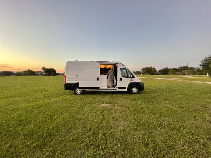 Freedom awaits with an RV rental! A person in their camper van, parked in a grassy field at sunset.