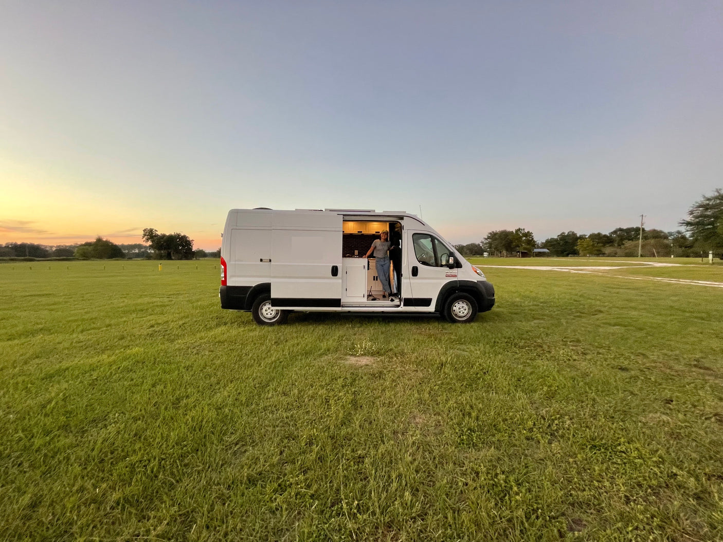 Freedom awaits with an RV rental! A person in their camper van, parked in a grassy field at sunset.