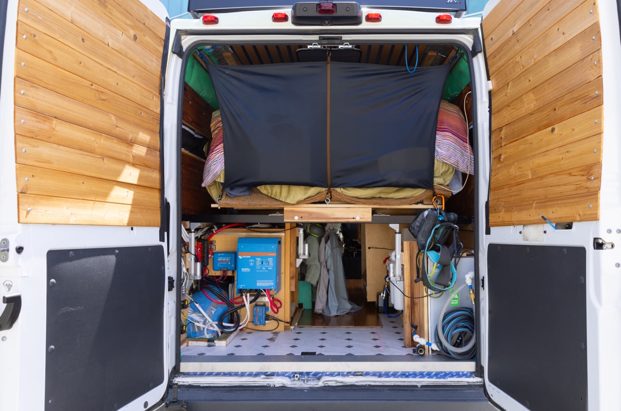 Explore a comfortable RV rental campervan conversion from the rear, revealing its cozy bed, electricals, and water system.