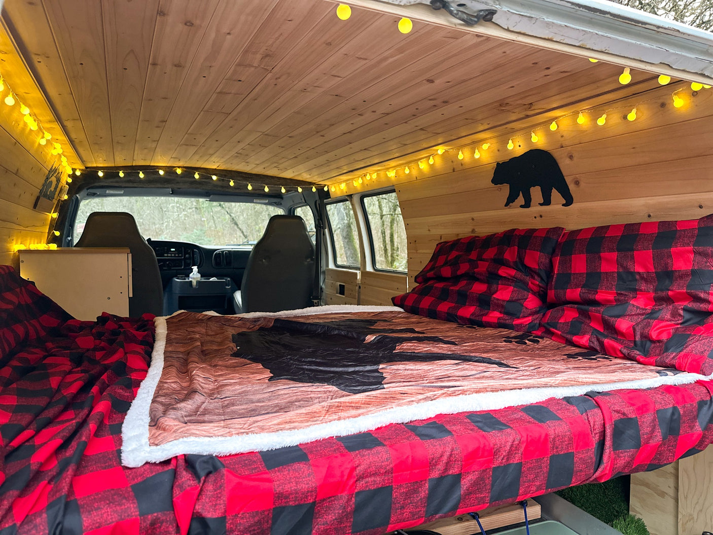 This inviting RV rental offers a cozy van life experience with a wood interior, buffalo plaid bedding, and bear accents.