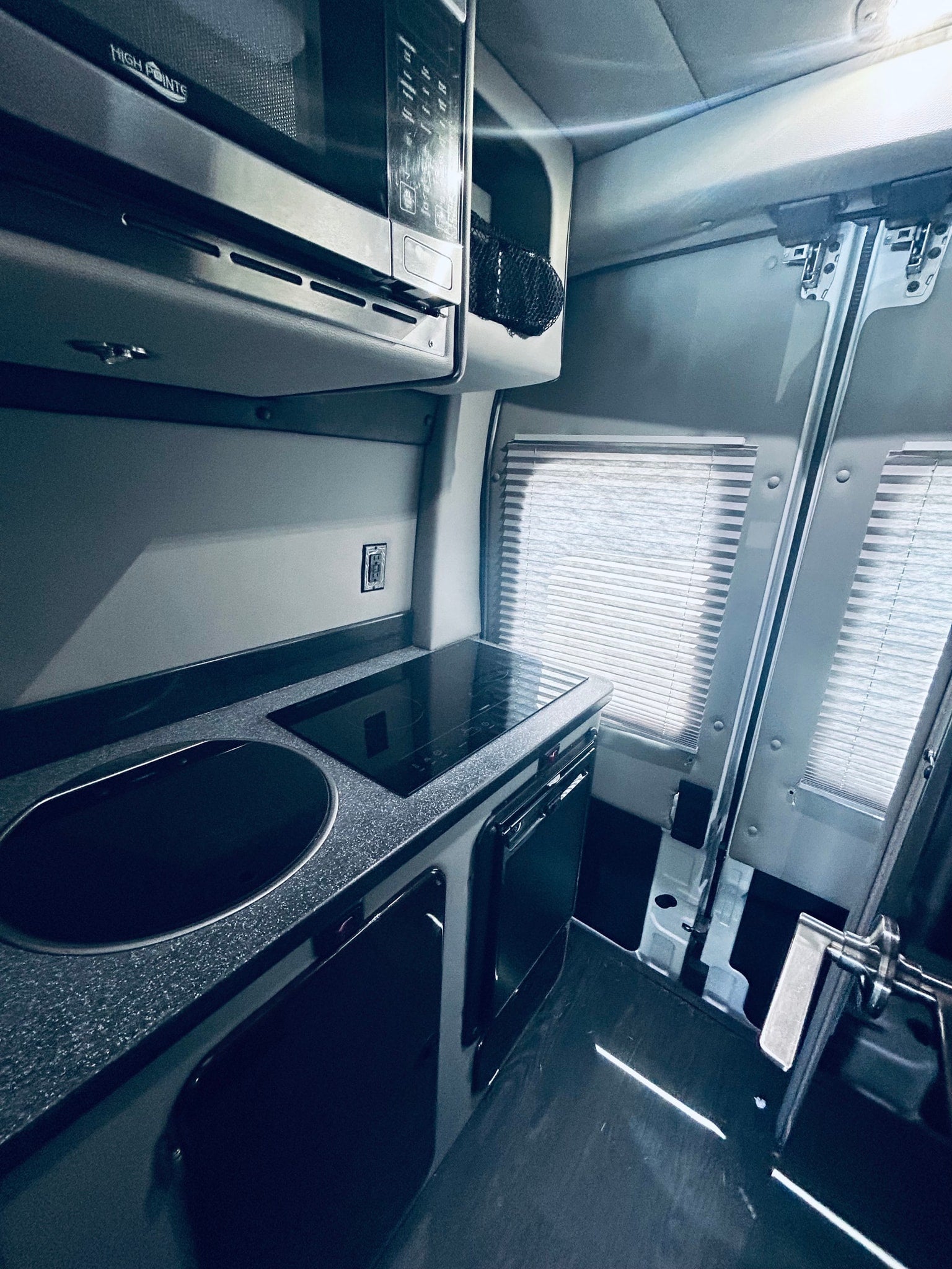 This rv rental features a compact, modern kitchen with a High Pointe microwave, sink, induction cooktop, and window blinds.