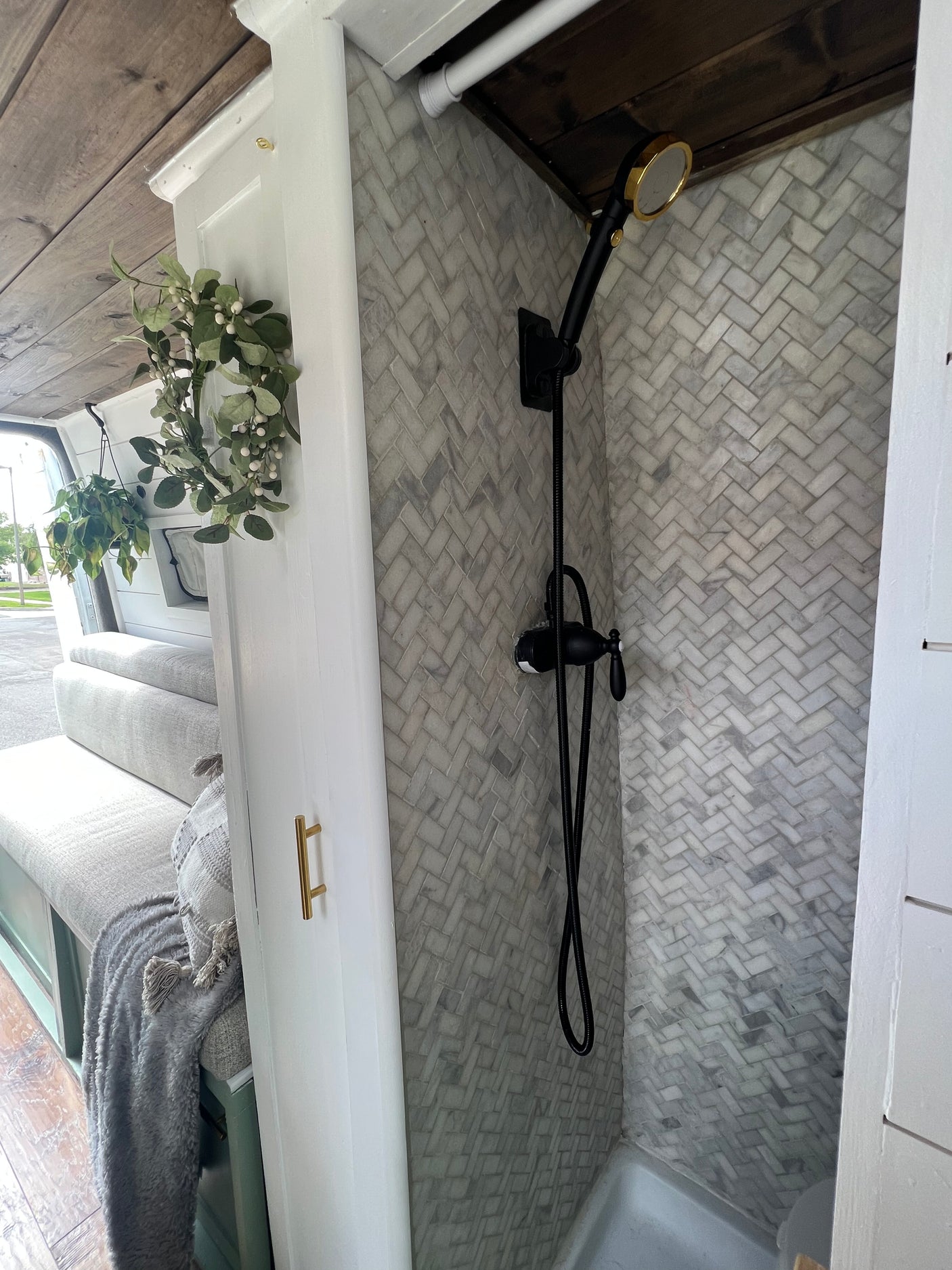 RV rental: Stylish interior showcasing a herringbone tiled shower with black and gold fixtures, and cozy bench seating.