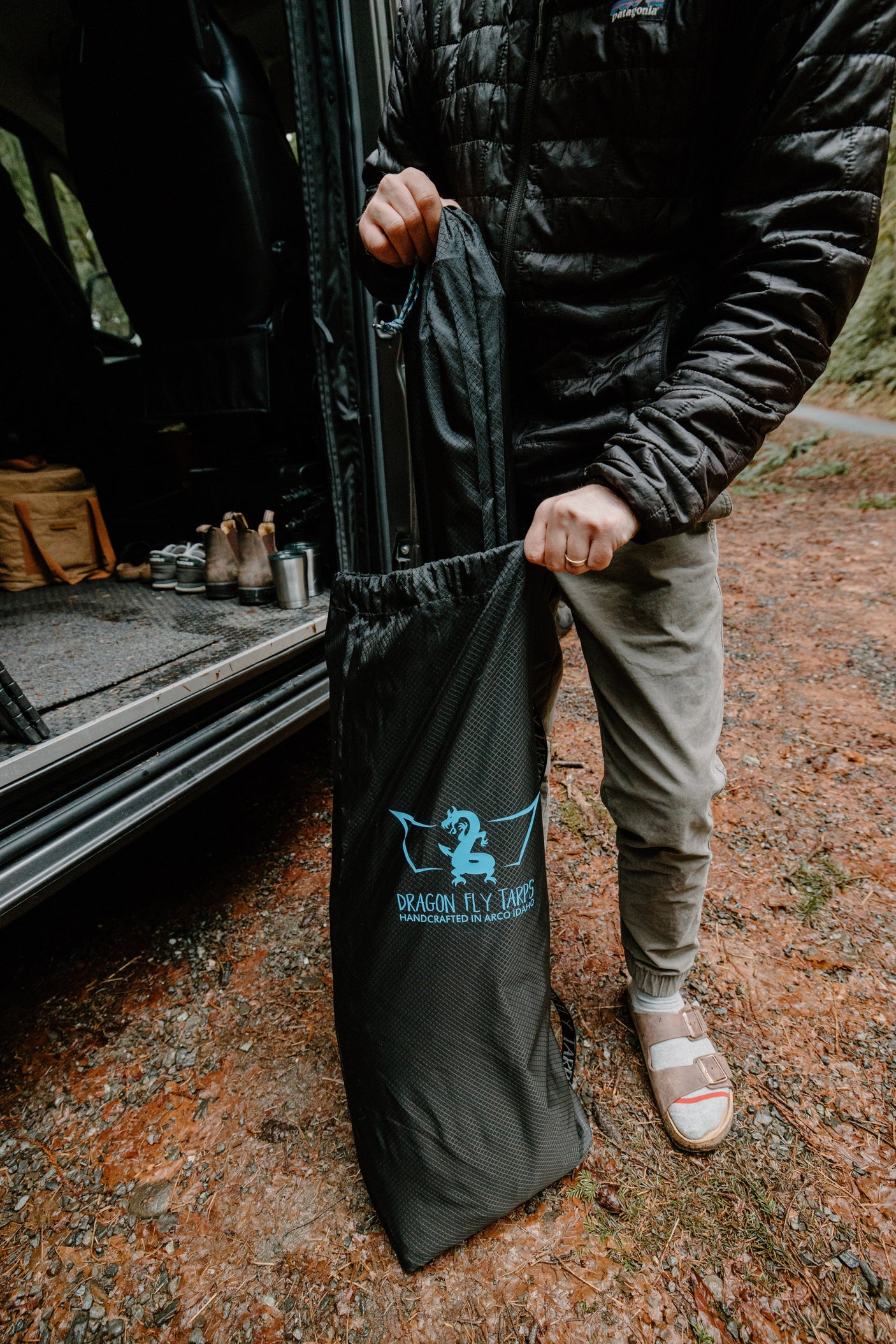 A person extracts a black Dragon Fly Tarps bag from an RV rental, preparing for an outdoor camping adventure.