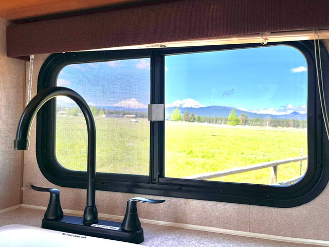 Enjoy scenic views from your RV rental kitchen! Black faucet overlooks green fields & snow-capped mountains under a blue sky.