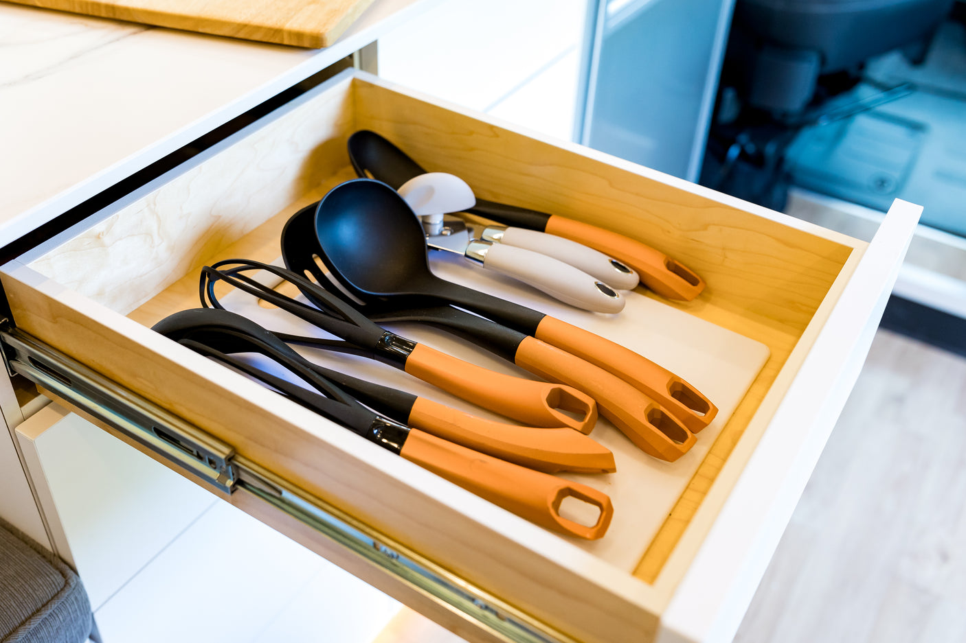 Essential kitchen utensils neatly stored in an open RV rental drawer, featuring black and orange handled spatulas and a ladle.