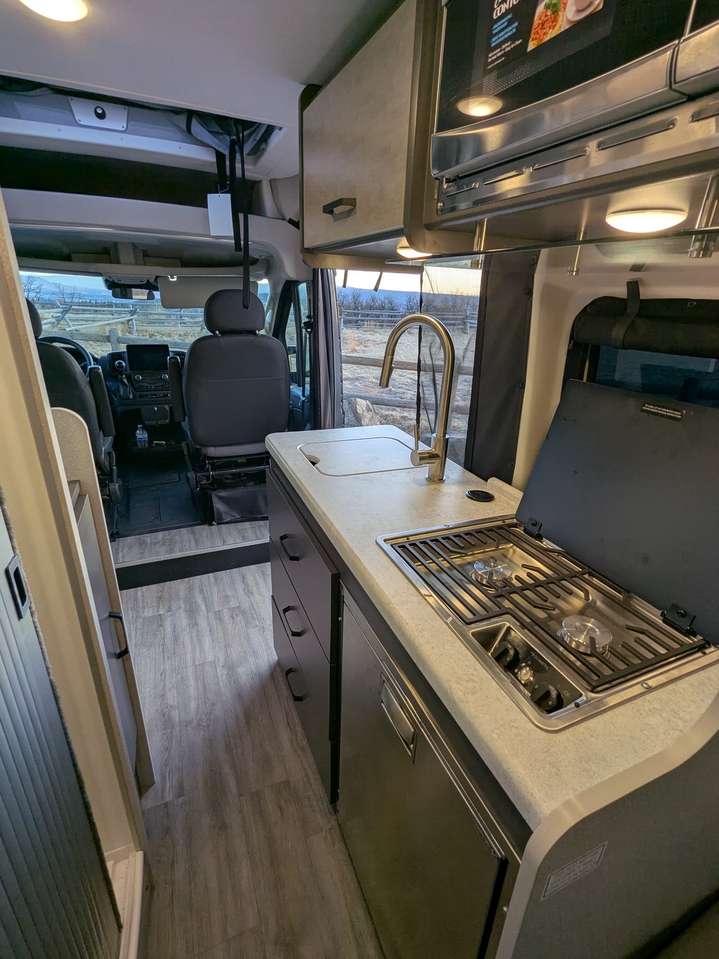 Interior view of an RV rental with a compact kitchen featuring a sink, Dometic stove, microwave, and front cockpit area.