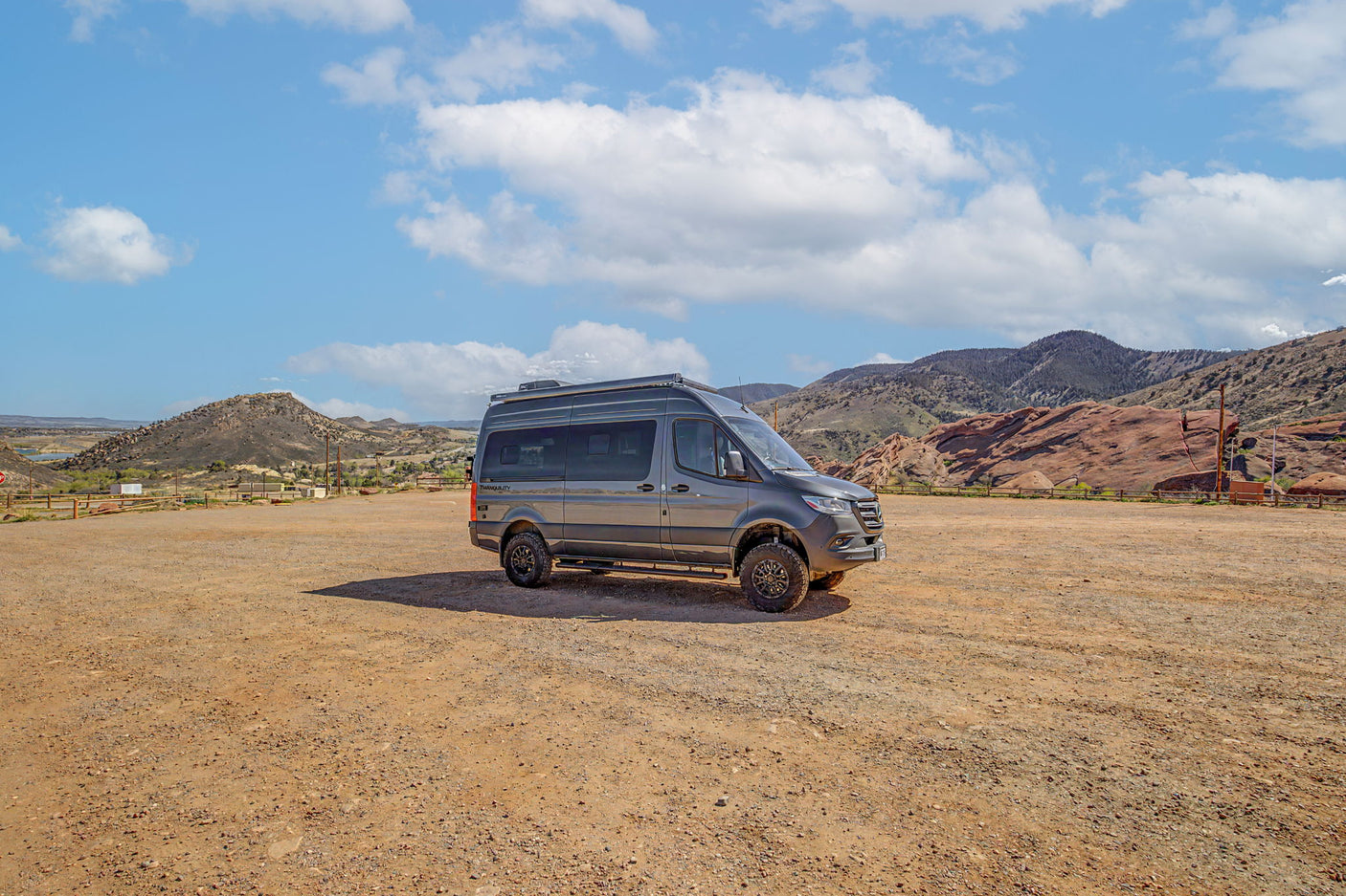 Adventure awaits! This rugged rv rental, parked on a dirt lot, is perfect for exploring mountains & deserts under a blue sky.