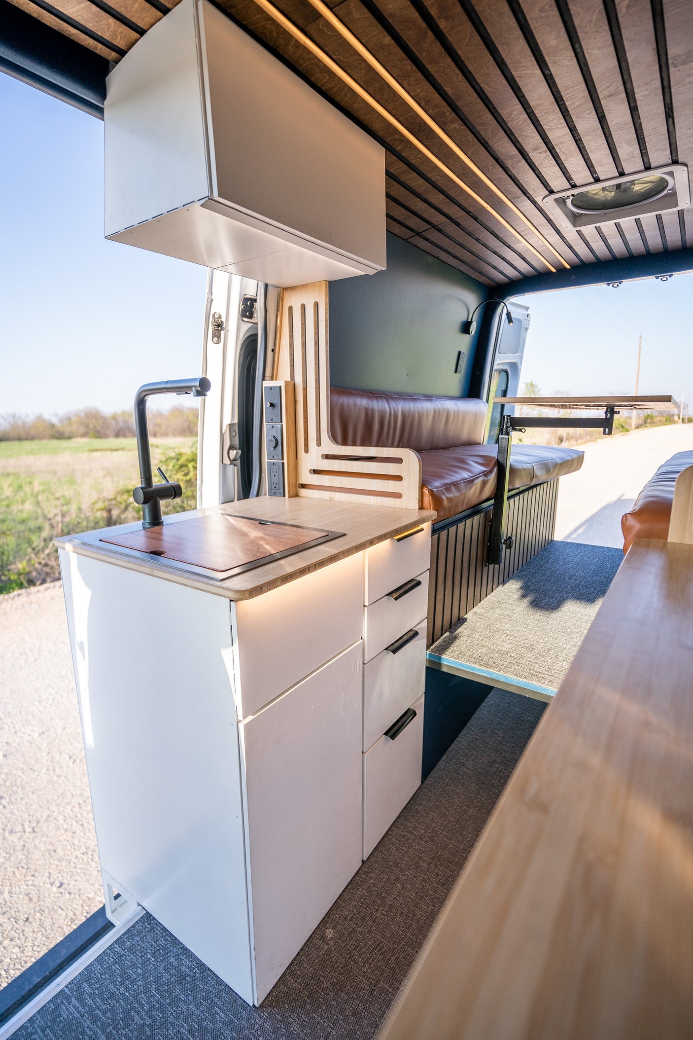 Inside a modern rv rental camper van: full kitchen, organized storage, comfortable seating, and wooden ceiling.