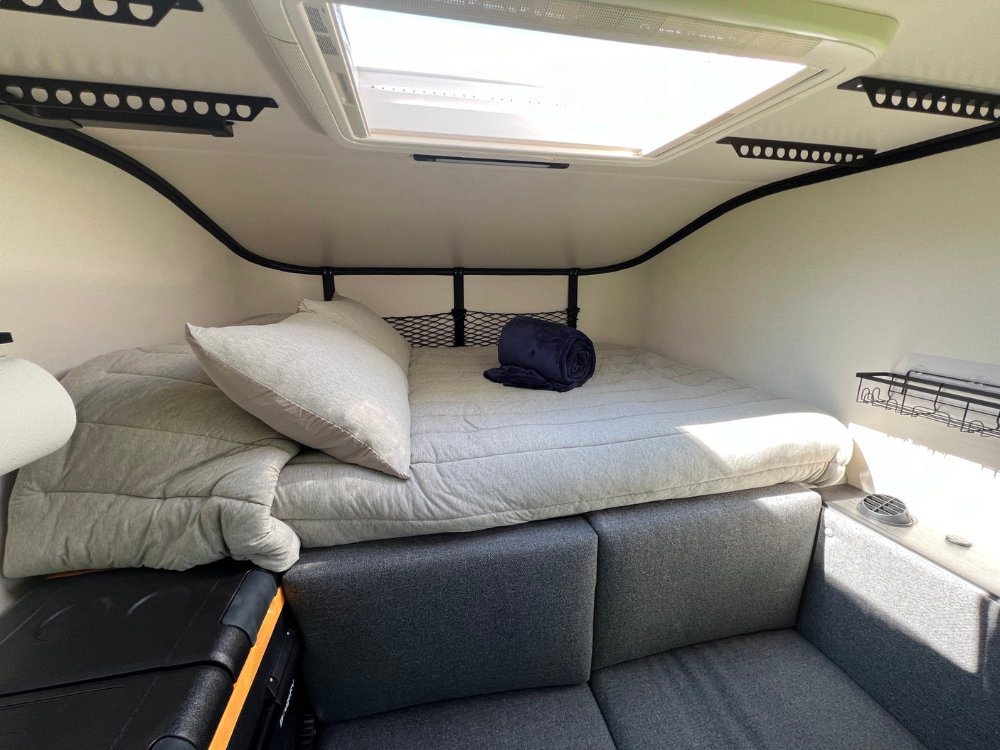 Inside a modern rv rental: a comfy bed, seating area, skylight, and storage. Ideal for road trip adventures.