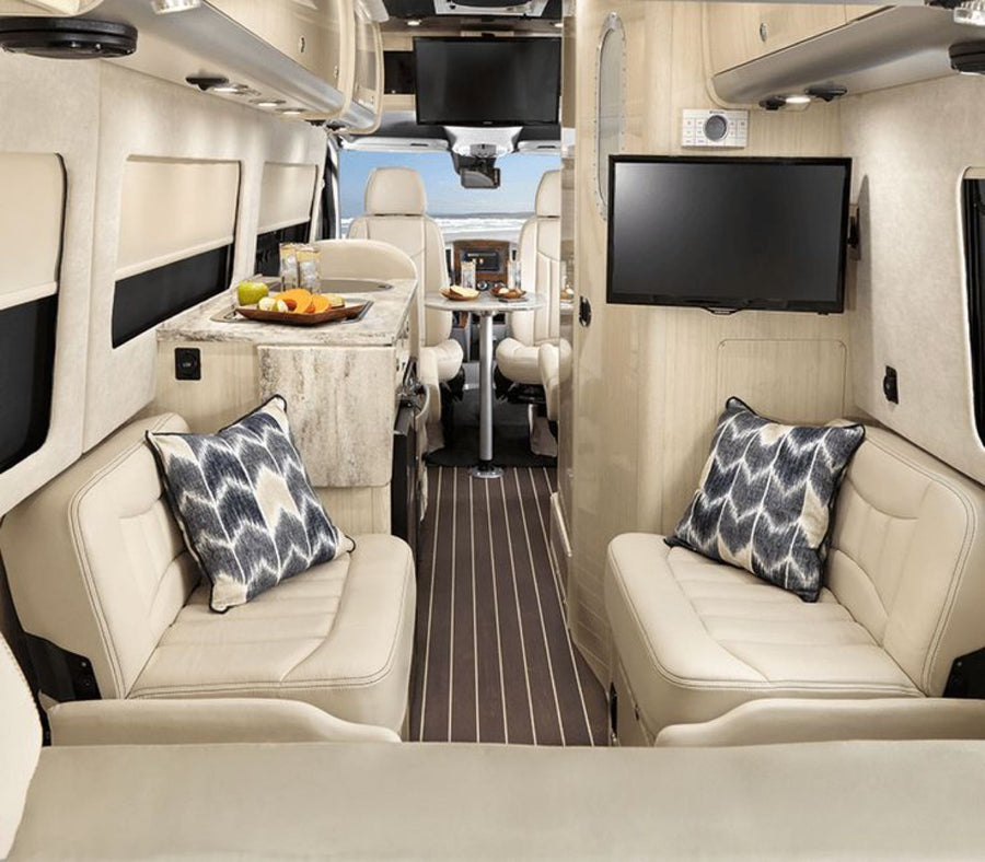 This luxury RV rental interior features comfy seating, a kitchen, TV, and a dining area, with a beach view through the front.