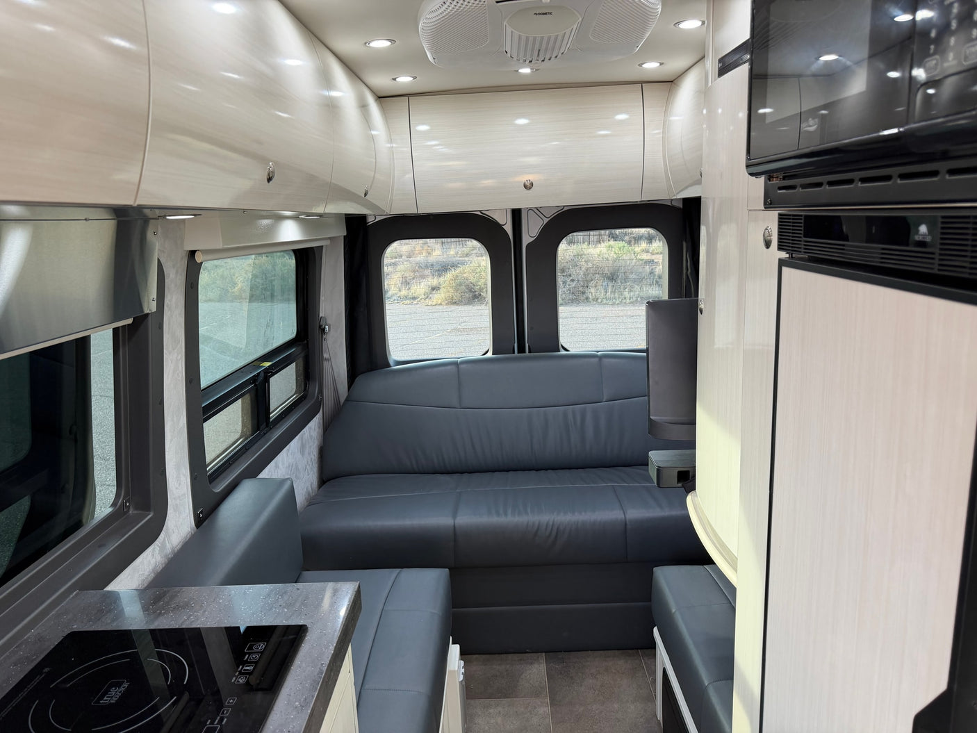 Modern rv rental interior: spacious living area with gray sofa, full kitchen, microwave, and overhead storage.