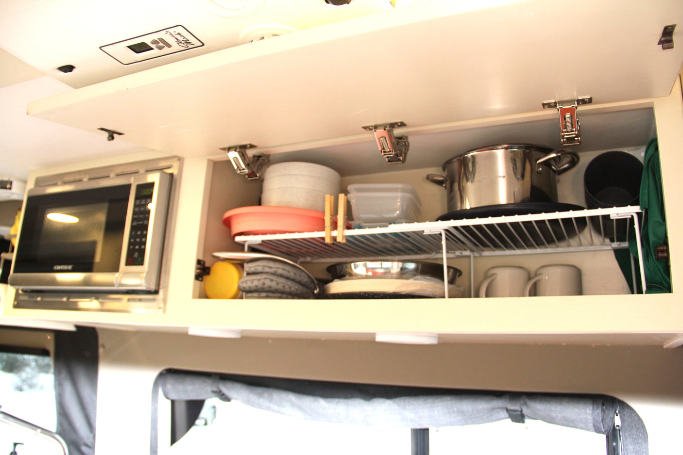 An open, organized overhead cabinet in an RV rental kitchen, with a microwave, pots, and dishes neatly stored.