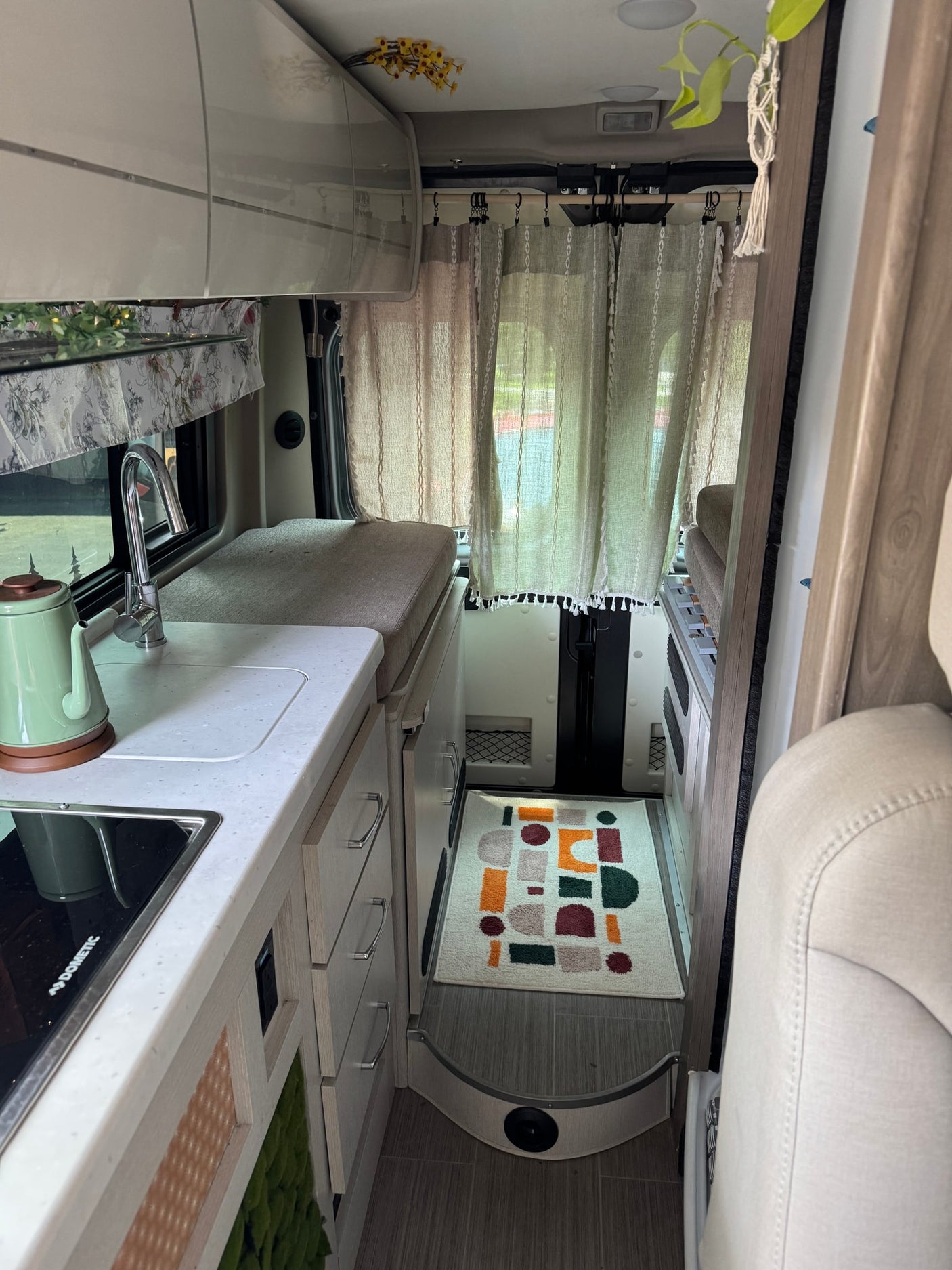 Bright rv rental interior with light wood cabinetry, a compact kitchen (sink, stovetop), cozy living space, & patterned rug.