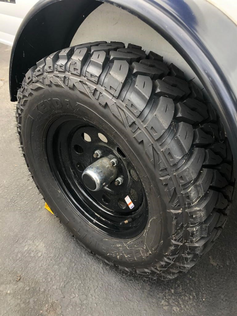 Close-up of a rugged tire with deep tread and a black rim, typical on an RV rental or travel trailer, ready for adventure.