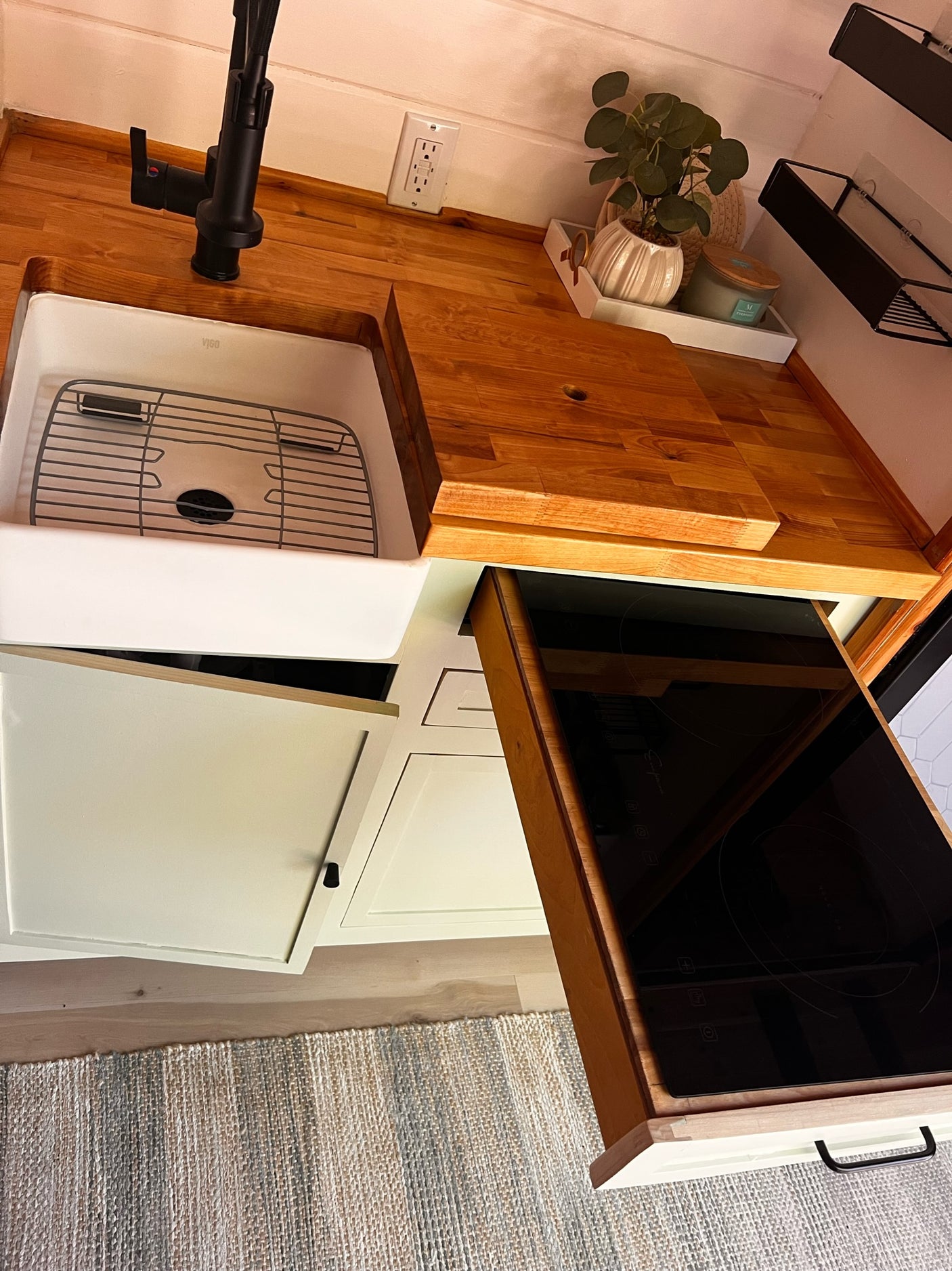 Modern RV rental kitchen featuring a pull-out induction cooktop, farmhouse sink, and light wood counters.
