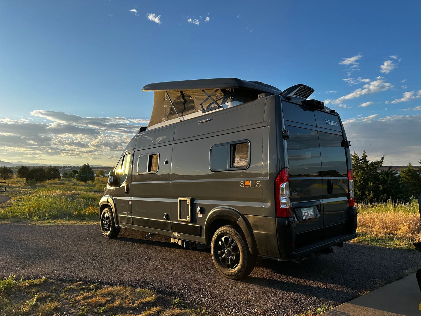 Grey Winnebago Solis camper van with pop-top extended, parked on asphalt in scenic outdoor setting. Perfect for an RV rental adventure.