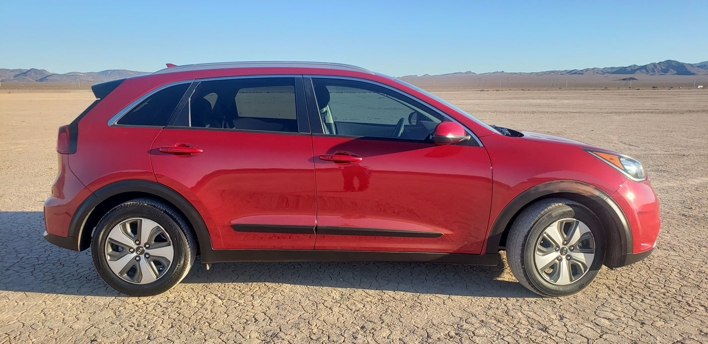 Red car, not an RV rental, on cracked desert ground with mountains under a clear sky. Ready for travel adventure.