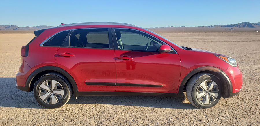 Red car, not an RV rental, on cracked desert ground with mountains under a clear sky. Ready for travel adventure.