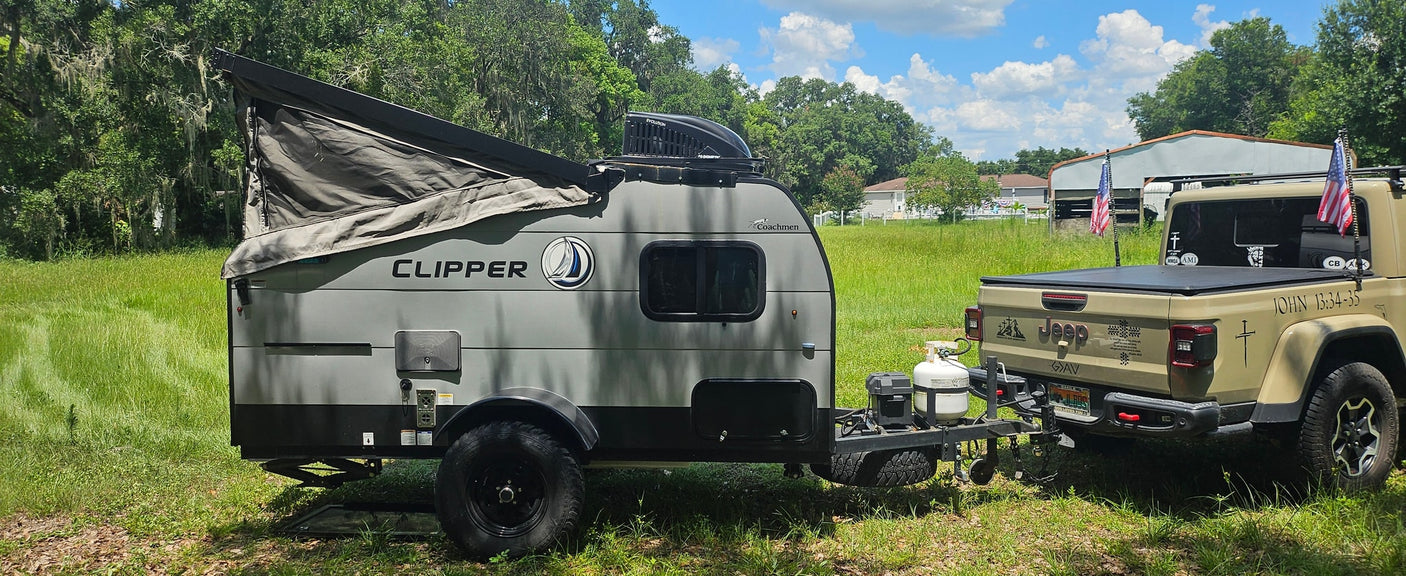 A gray Coachmen Clipper pop-up travel trailer hitched to a tan Jeep Gladiator. Ideal RV rental for off-road camping adventures.
