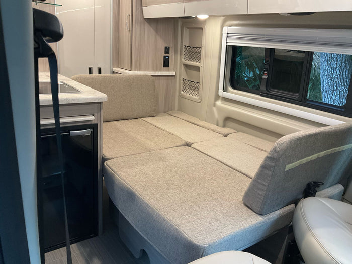 RV rental interior featuring a versatile bed/seating area, compact kitchenette, and window with outdoor views.