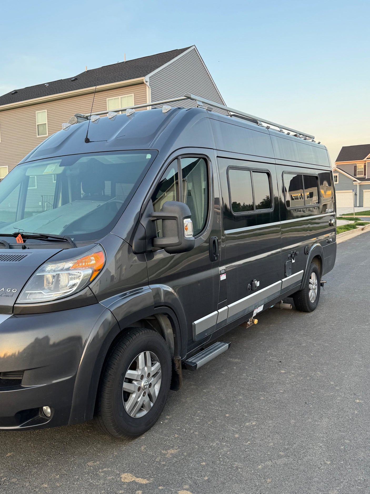 Dark grey Winnebago camper van, perfect for rv rental getaways, parked on a quiet residential street in soft evening light.