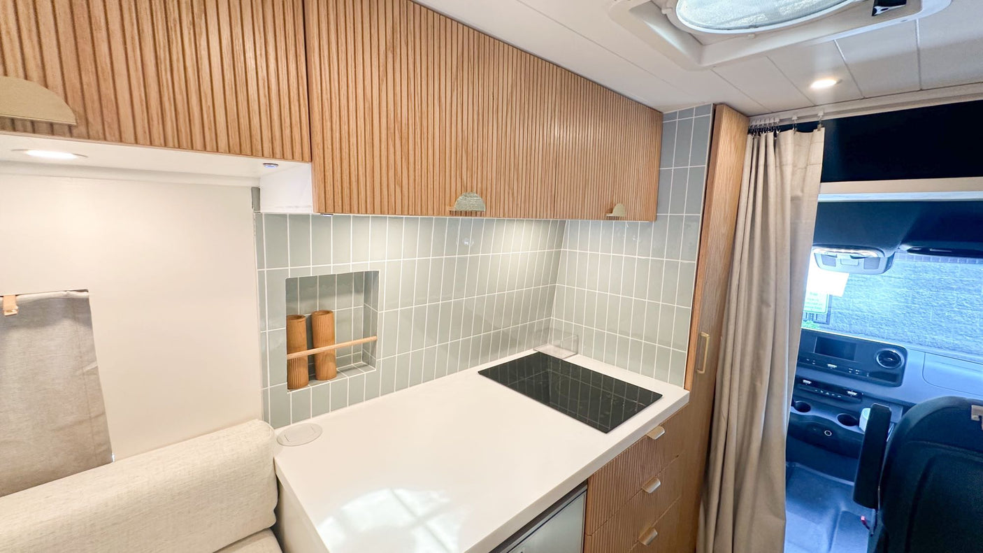 wooden cabinets & table are visible.|White Mercedes Sprinter RV rental van with roof rack & ladder