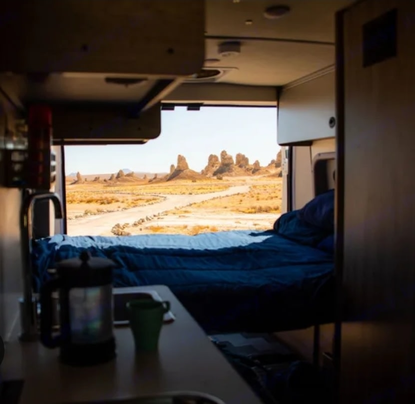 Wake up to amazing views! An RV rental offers a bed, coffee, and a panorama of desert rock formations from its open back.
