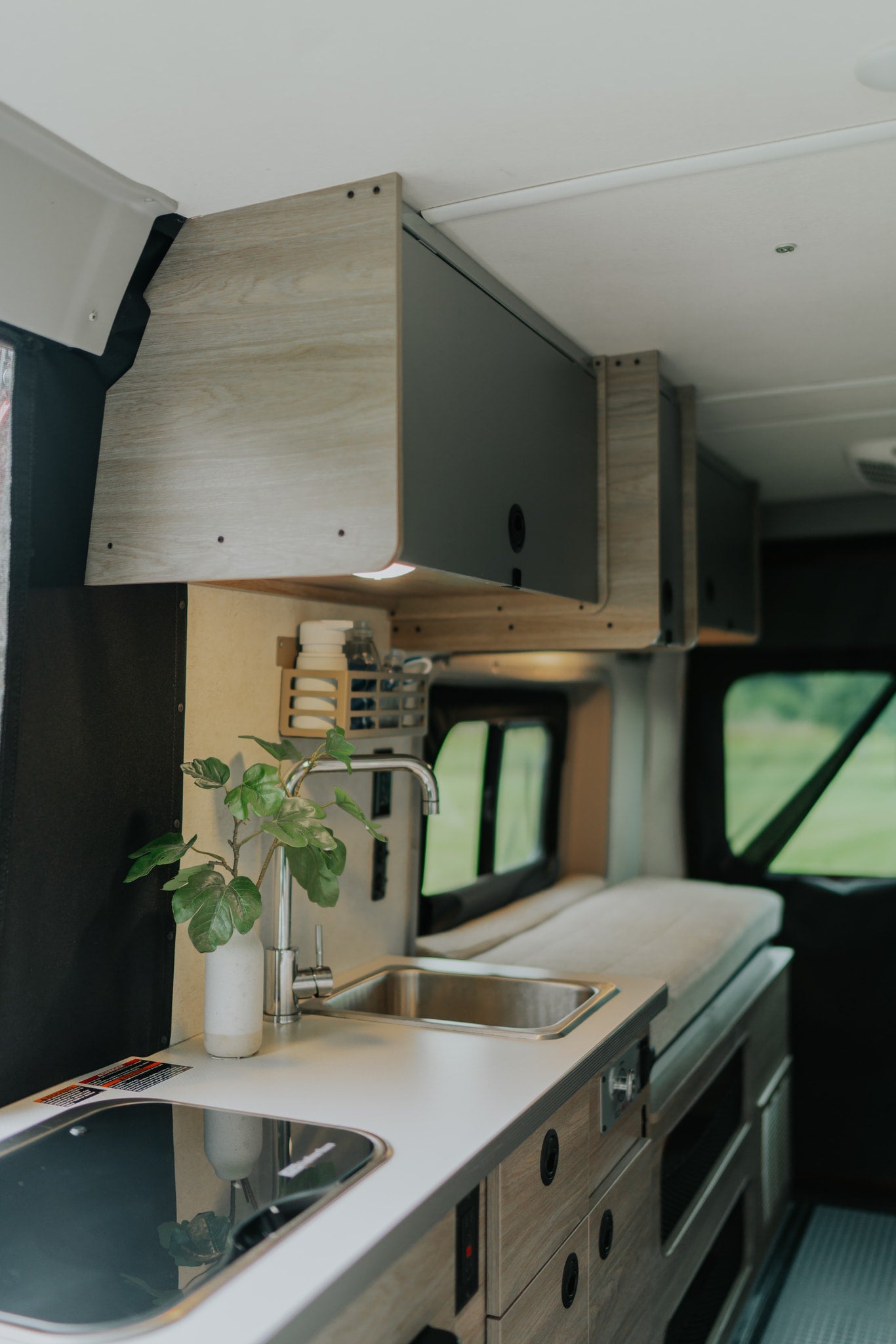 Modern RV rental interior: compact kitchen with sink & cooktop, overhead storage, and bed area for travel comfort.