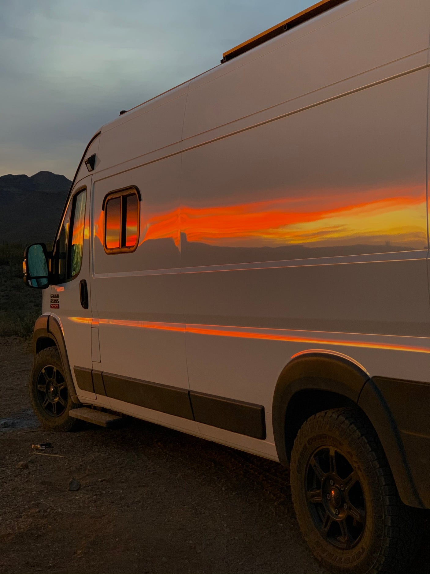 Stunning sunset reflecting vibrantly off a white RV rental, parked in a serene mountain desert.