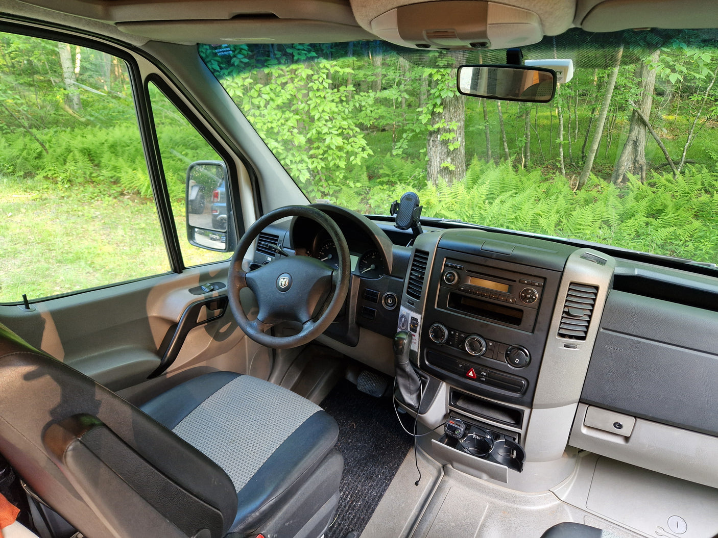 Driver's view from an rv rental: a detailed look at the van's cockpit, dashboard, and vibrant forest outside.