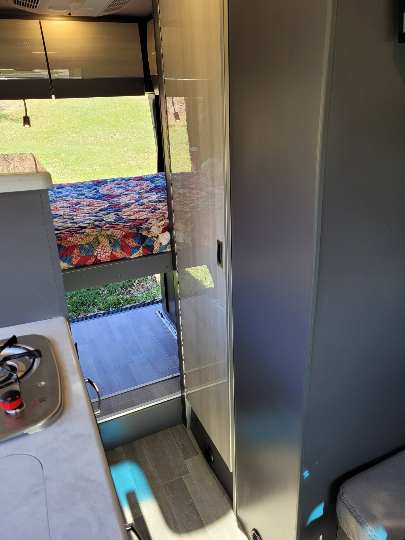 This RV rental features a cozy bed, compact kitchen, and an open rear ramp to the outdoors. Perfect for adventure.