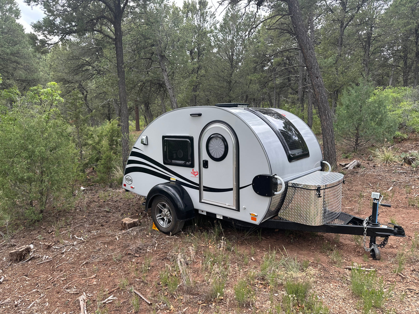 A compact RV rental teardrop trailer parked in a serene forest setting, perfect for outdoor camping trips.
