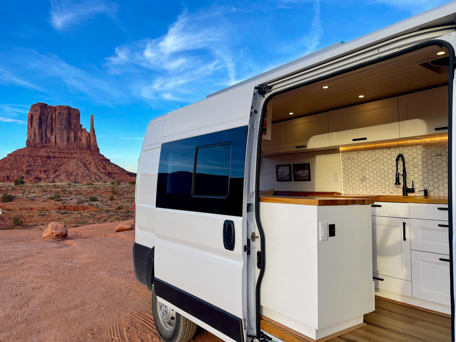 White RV rental with open side door showcasing its modern kitchen, parked in the red desert of Monument Valley.