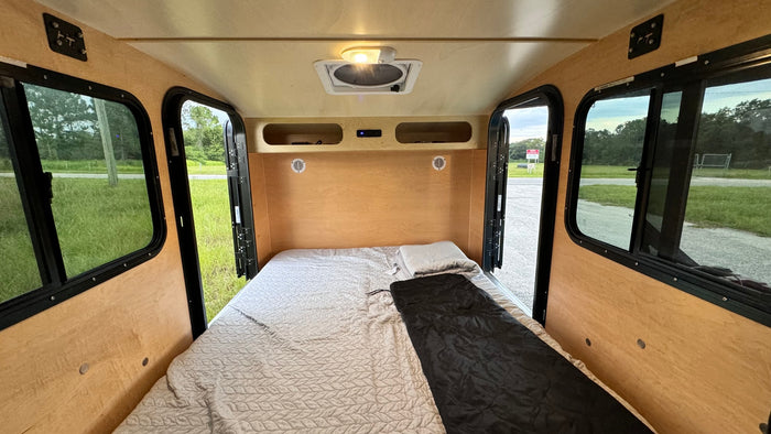 and a table on a blue mat in a grassy field.|An RV rental's inviting interior: a comfortable bed