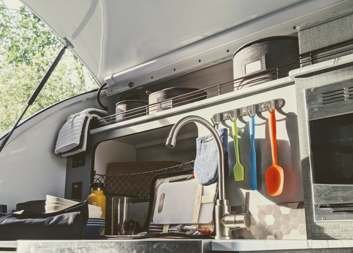 Well-equipped RV rental outdoor kitchen: sink, colorful utensils, storage, and microwave. Great for glamping!