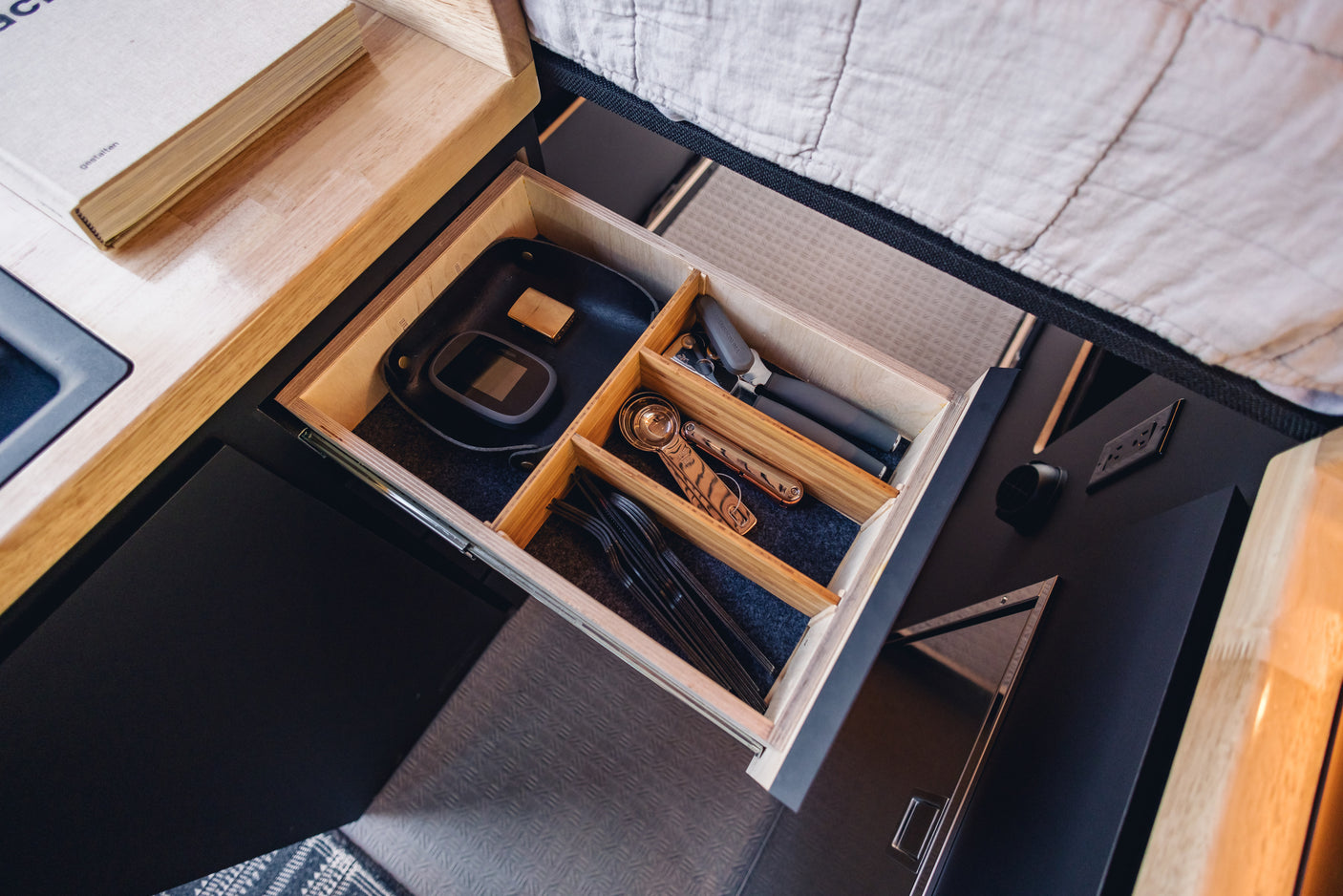 RV rental: An open, organized wooden drawer with black felt lining, holding kitchen utensils and tech, showcasing clever compact storage.