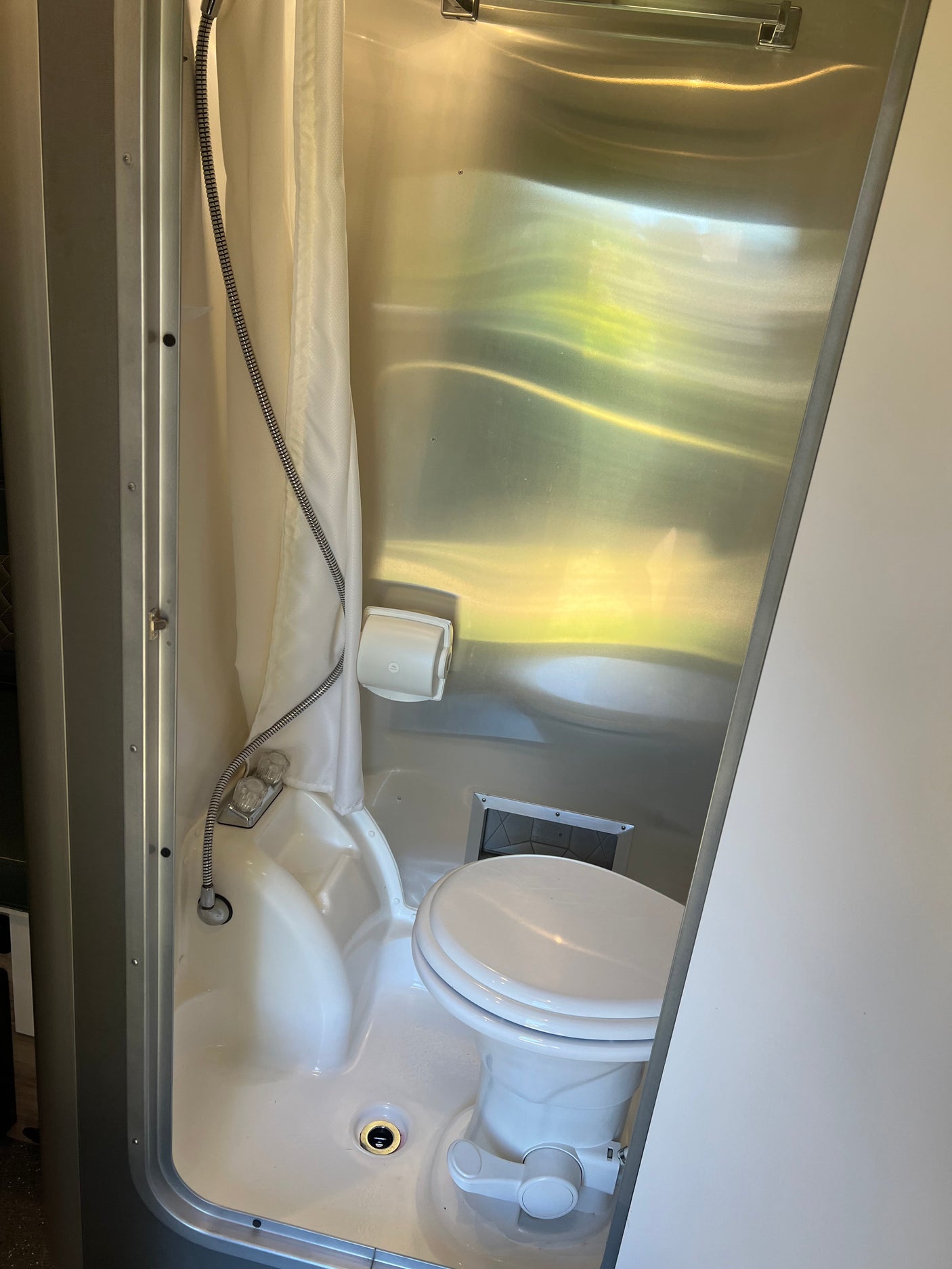 Clean RV rental bathroom featuring a wet bath with shower, toilet, and drain.