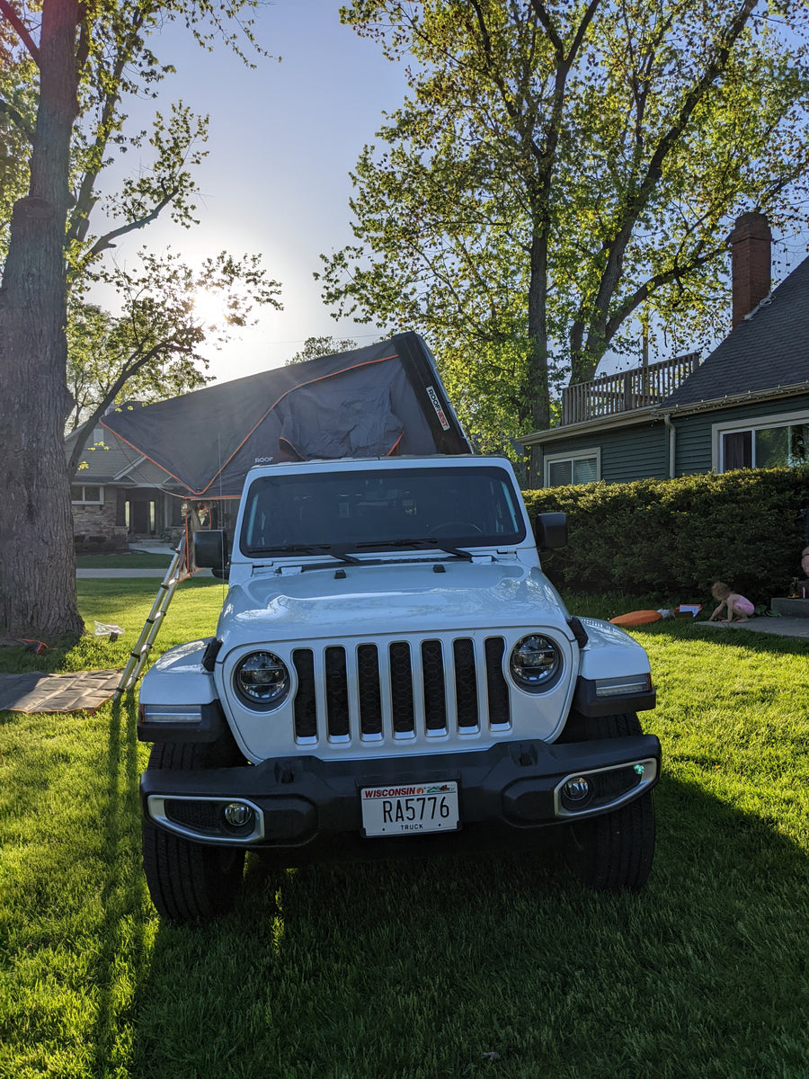 offering an RV rental-like experience.|White Jeep Gladiator with a deployed rooftop tent & ladder on a lawn