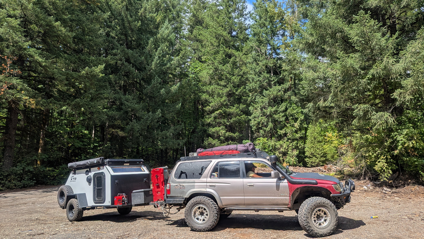 Off-road SUV towing an overland camping trailer through a dense forest. A rugged RV rental option for adventure travel.