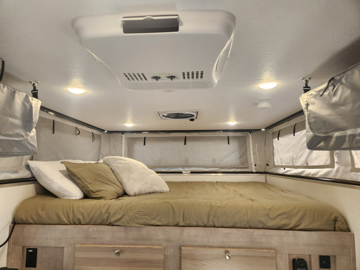 Inside an RV rental: a comfortable bedroom with a made bed, AC, ceiling fan, and soft-sided sleeping area.