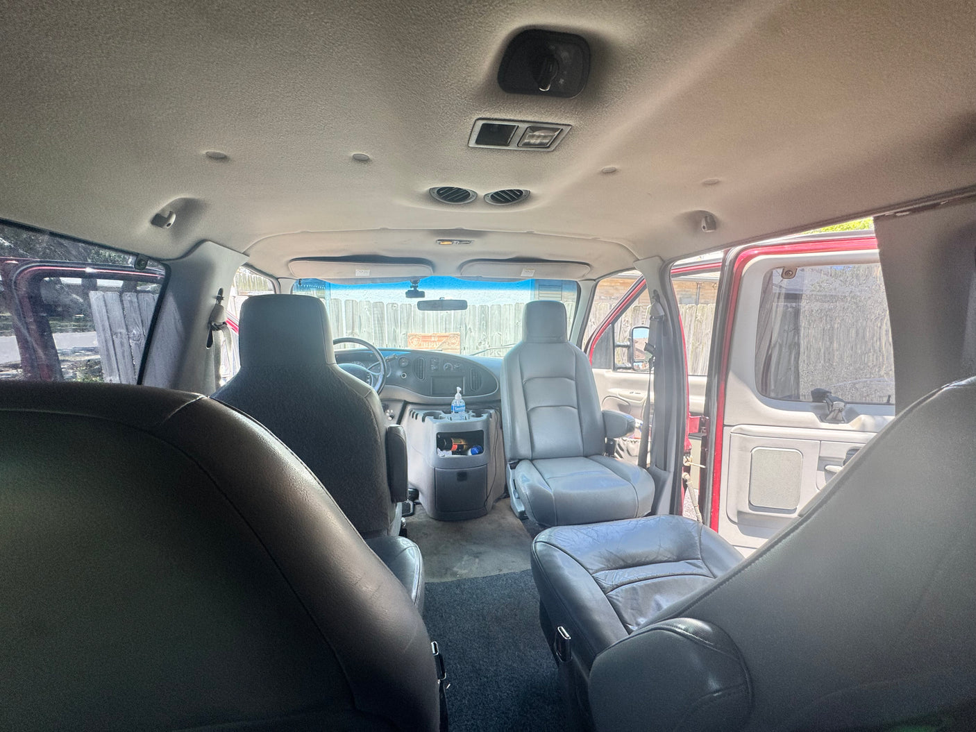 Interior view of an **rv rental** van with gray seats, visible dashboard, overhead controls, and open side doors letting in natural light.