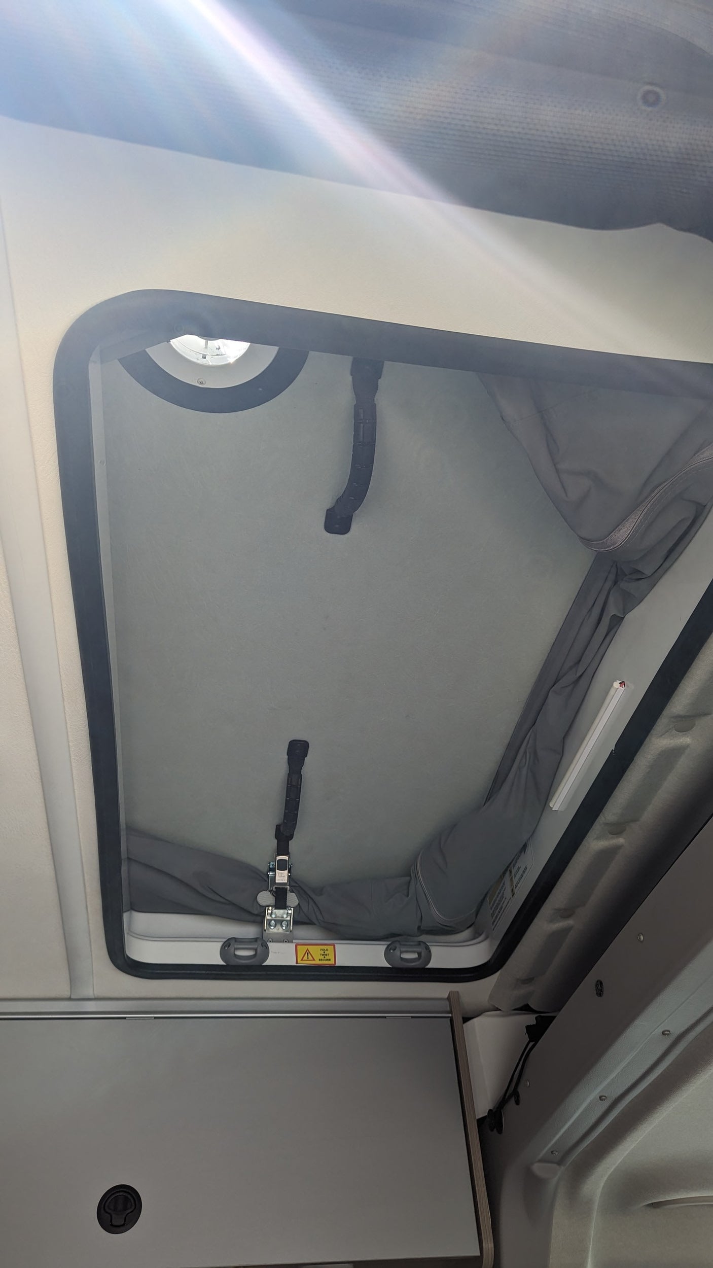 Inside an RV rental: a bright pop-top roof with grey fabric walls, overhead light, and secure latches. Ideal for camper adventures.
