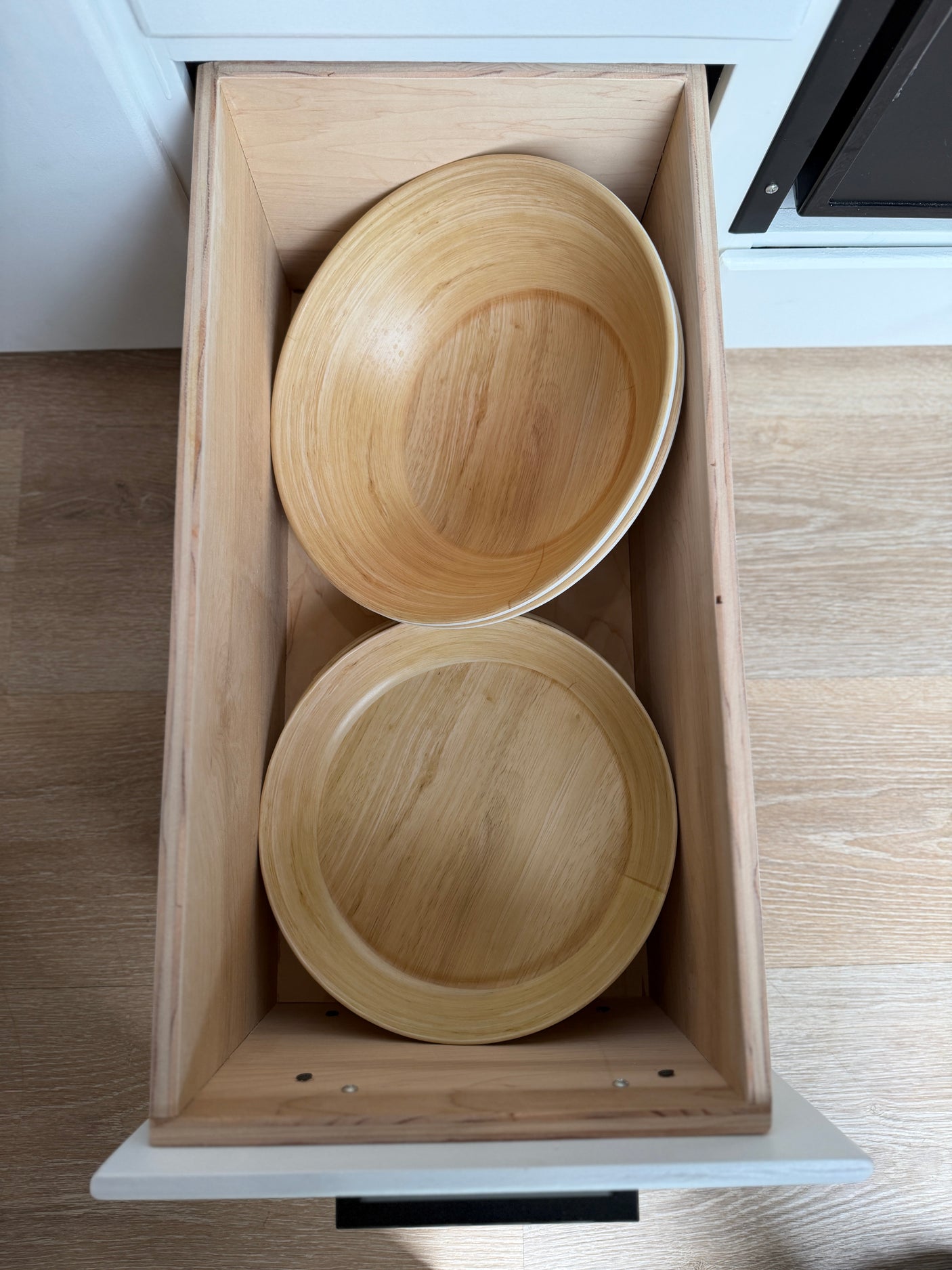 Open RV rental drawer reveals organized kitchen storage: a light-colored wooden bowl stacked above a matching plate.