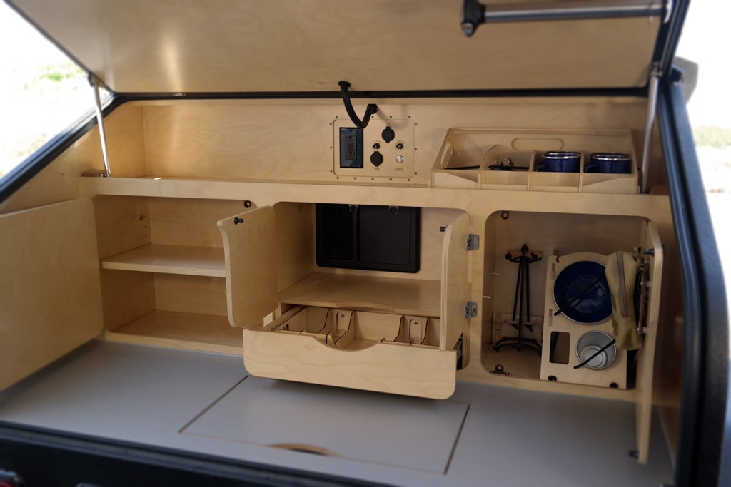and stemware storage in a compact camper interior.|RV rental interior: Wooden power panel with voltmeter