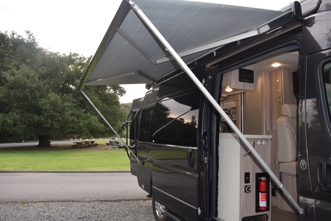 An rv rental camper van with its awning extended, showcasing a cozy interior with kitchen & essential amenities.